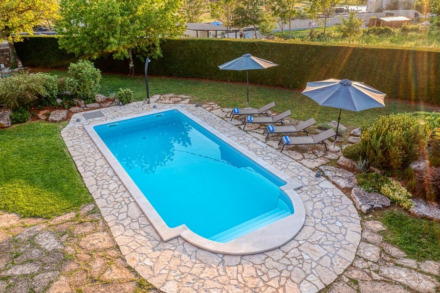 Pool med solstolar, parasoller och gräsmatta
