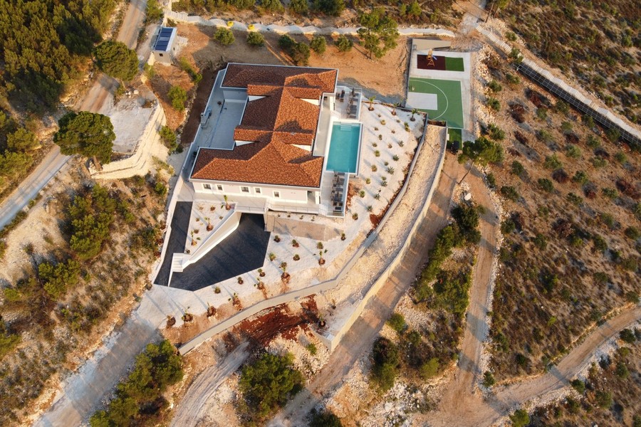 Flygfoto över villan med pool och sportplan